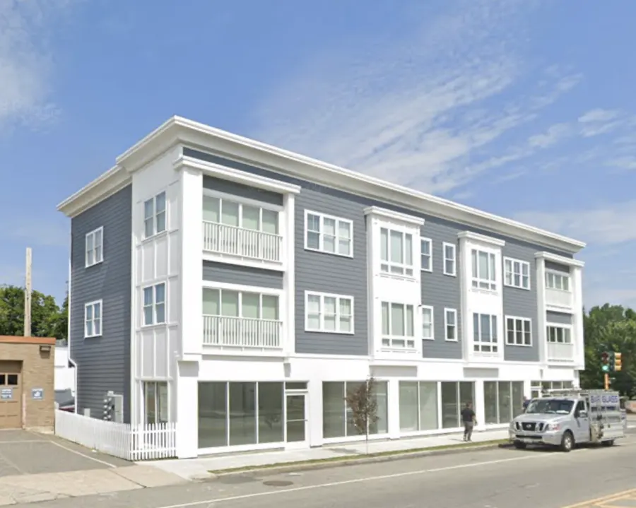 A new three-storey building at 887 Massachusetts Avenue, built out to the sidewalk with no front setback and a single young street tree beside it.
